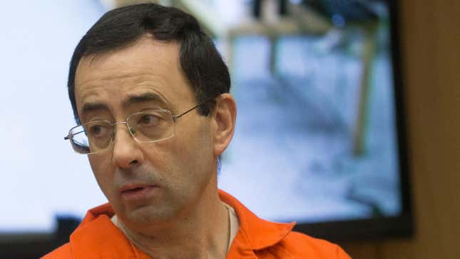 A white man with dark hair glasses in an orange jumpsuit looks away from the camera in a courtroom.